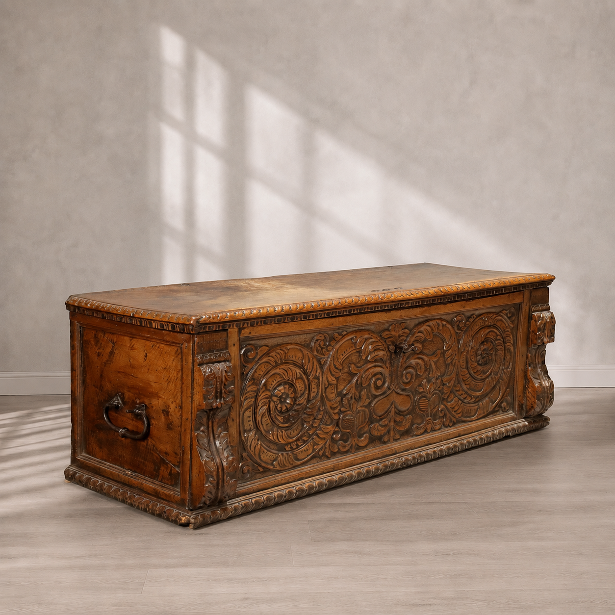 Antique hand-carved walnut cassone chest with elaborate Renaissance acanthus scrollwork relief carvings, iron side handles, and egg-and-dart molding along the lid and base.