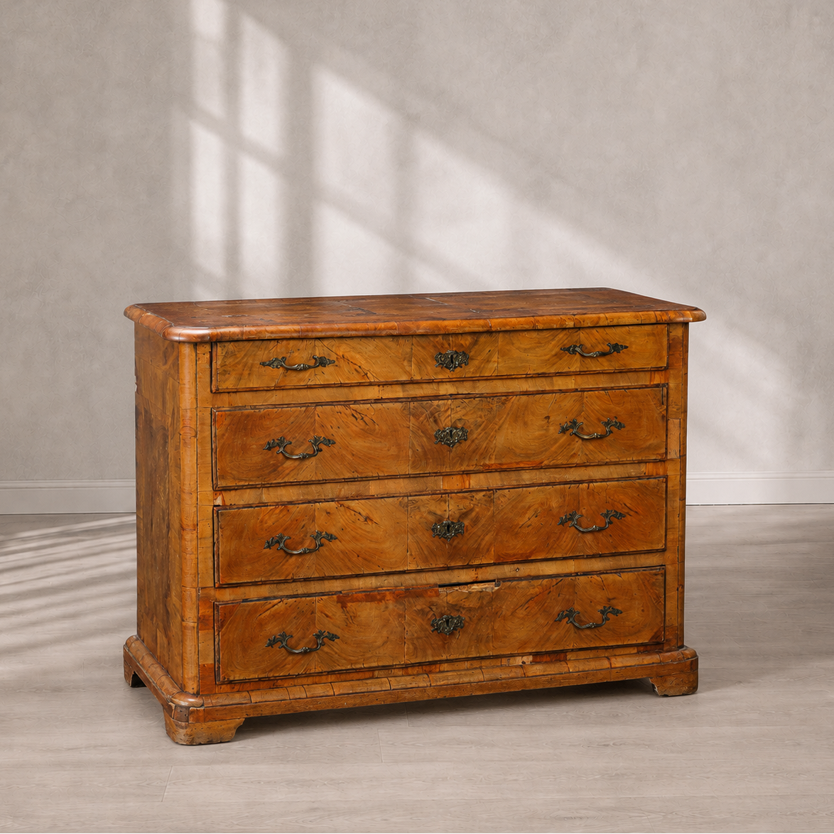 Antique four-drawer chest in warm honey walnut with burled wood veneer panels, ornate brass drop handles, bracket feet, and rounded corner molding details.