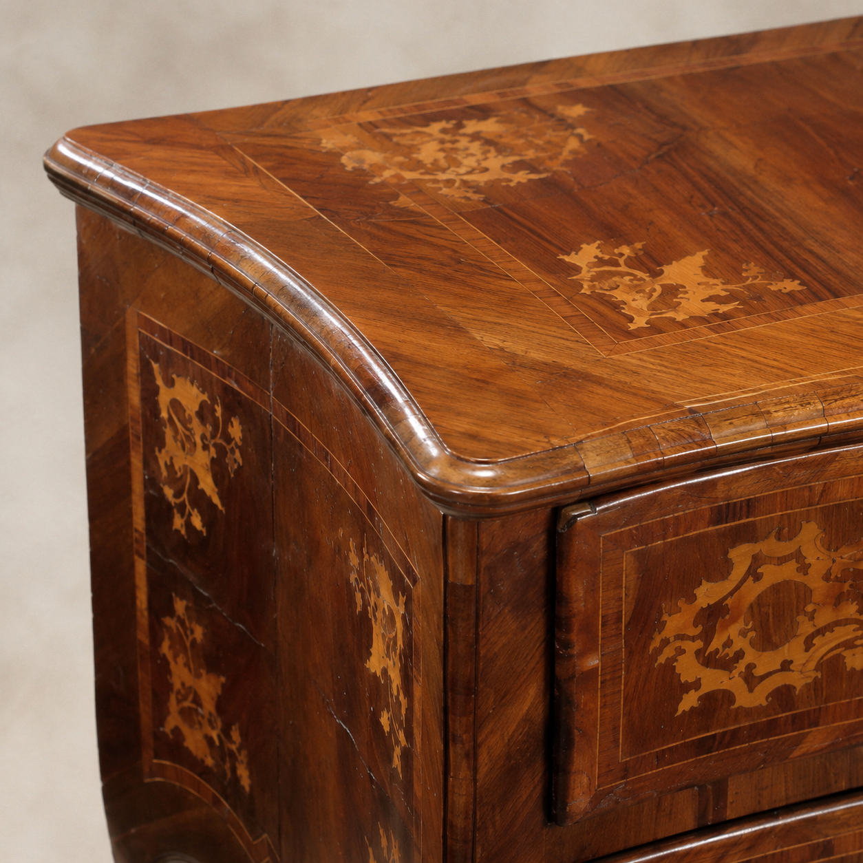 Antique Italian-style walnut chest with intricate lighter wood marquetry inlay featuring scrolling floral motifs, curved bombé form, and crossbanded top with molded edge.