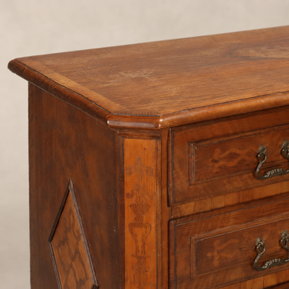 Antique walnut chest of drawers with marquetry inlay, ornate brass drop handles, raised panel sides, and rich warm brown patina showing traditional craftsmanship