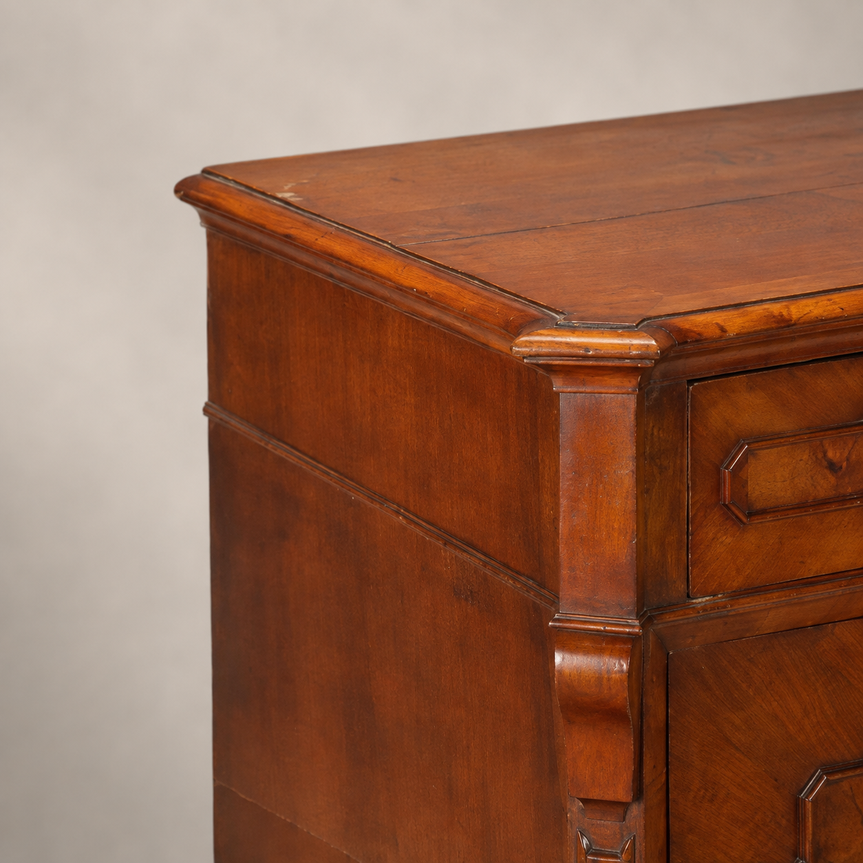 Antique walnut chest of drawers with rich warm brown finish, carved corner pilasters, geometric drawer pulls, and elegantly molded top edge, showcasing traditional craftsmanship.