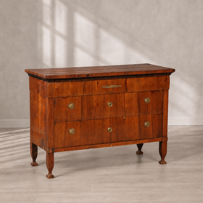 Antique cherry wood chest of drawers with three drawers, brass oval handles and keyhole escutcheons, reeded corner columns, tapered legs, and decorative brass inlay on top drawer.