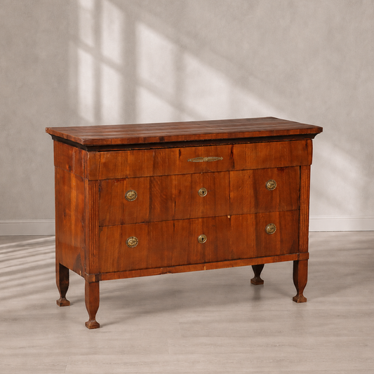 Antique cherry wood chest of drawers with three drawers, brass oval handles and keyhole escutcheons, reeded corner columns, tapered legs, and decorative brass inlay on top drawer.