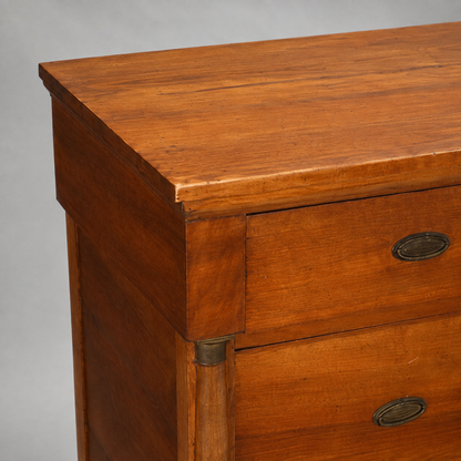 Antique walnut chest of drawers with warm honey-brown finish, oval brass hardware pulls, and fluted column detailing with brass cap accents on corners.