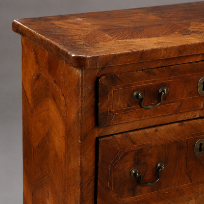 Antique walnut chest of drawers with herringbone parquetry top, decorative inlay panels, brass bail pull handles, and escutcheon keyhole plates on two visible drawers.