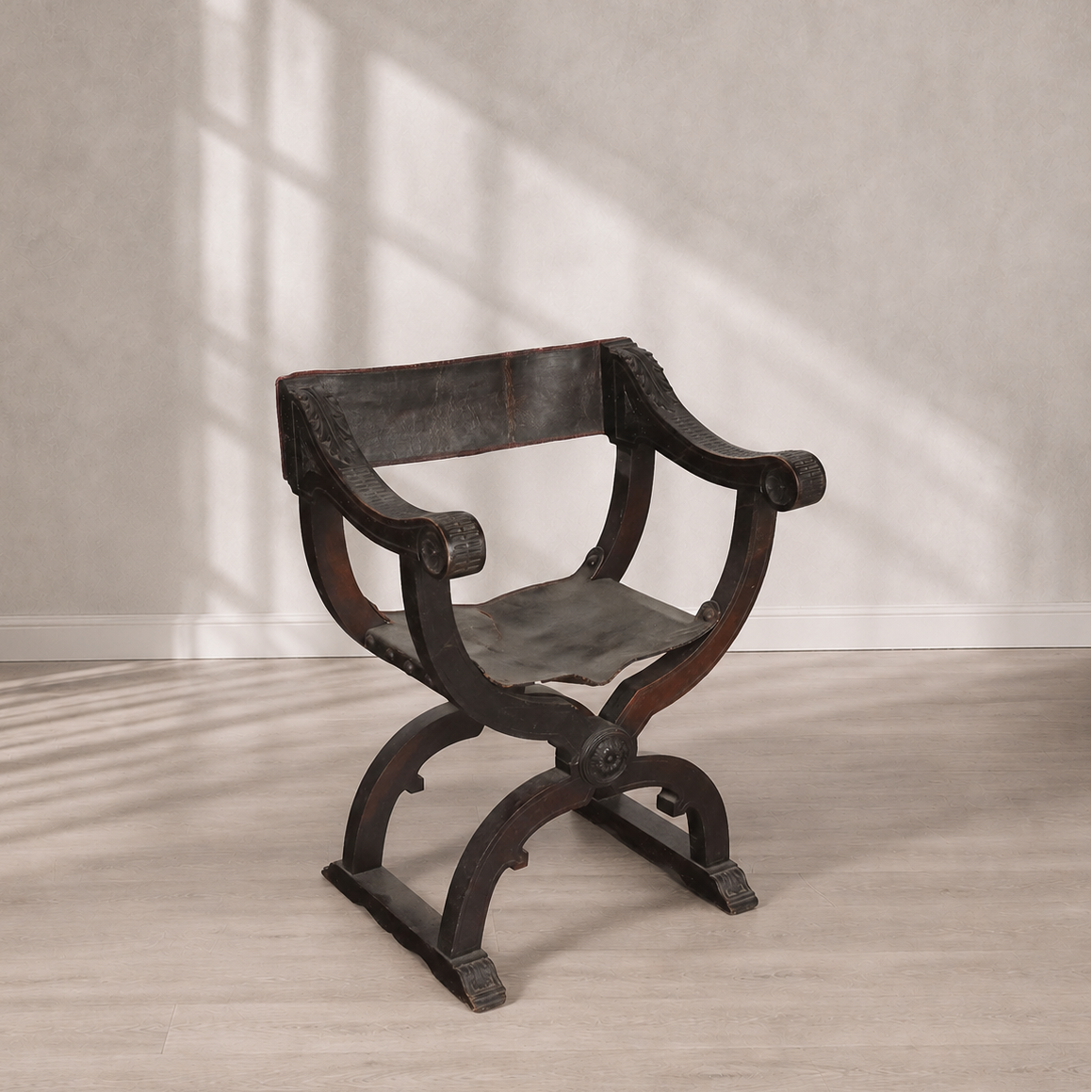 Antique Savonarola X-frame armchair in dark walnut wood with aged black leather seat and back, featuring carved scroll arms and ornate medallion details.