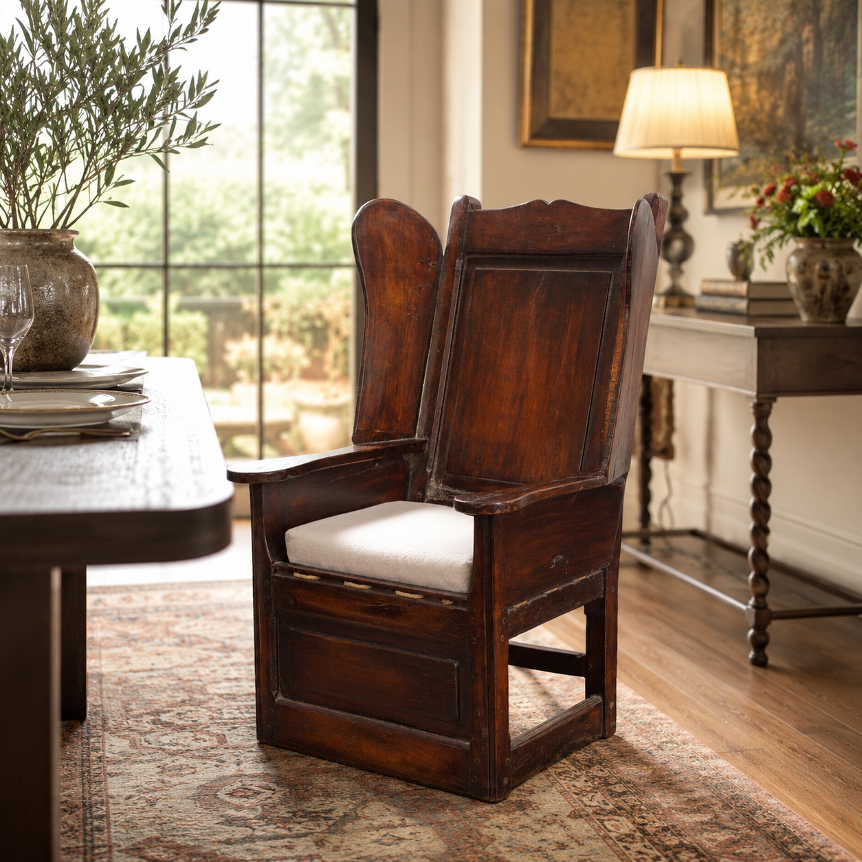 Antique wingback armchair in dark walnut wood with paneled back, carved details, worn distressed finish, and loose cream upholstered seat cushion