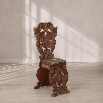 Ornately hand-carved dark walnut wood chair with baroque scrollwork, heraldic shield motif on backrest, claw feet, and intricate relief carvings throughout frame and seat.