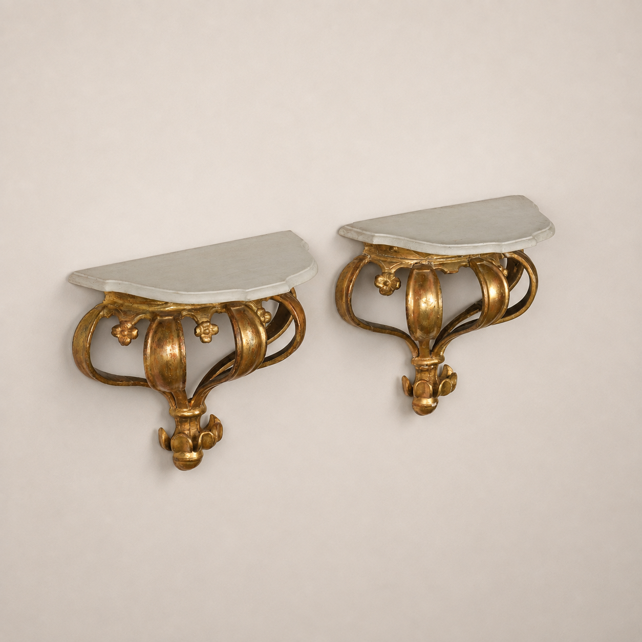 Pair of ornate Baroque-style gilded wall bracket shelves with white painted demi-lune tops, featuring scrolled acanthus leaf bases with floral accents in antique gold finish