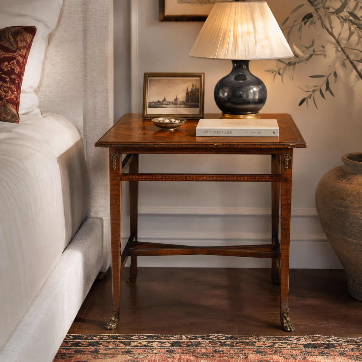 Antique-style walnut side table with brass claw feet, inlay detailing, cross stretcher base, topped with a dark ceramic lamp, framed photo, and book.