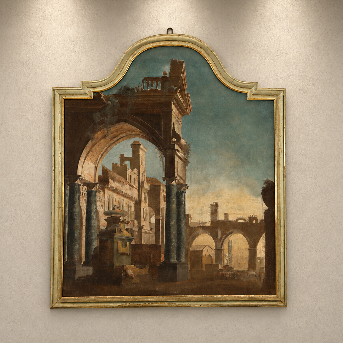 Antique capriccio oil painting in ornate arched frame depicting Roman ruins with classical arches, columns, and architectural fragments in warm earth tones and teal sky.