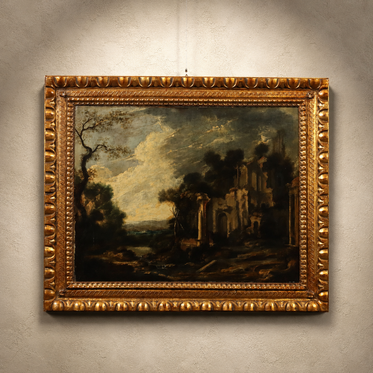 Antique oil painting in ornate gold gilt frame depicting dark romantic landscape with classical ruins, bare trees, and dramatic cloudy sky in muted earth tones.