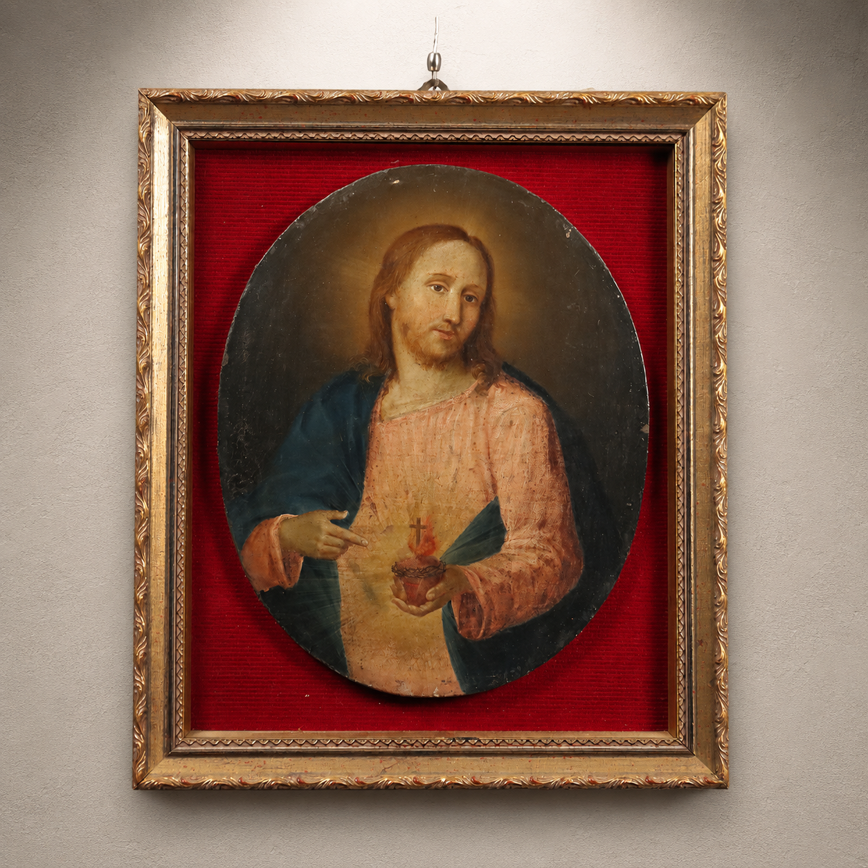 Antique oval religious painting of Sacred Heart of Jesus in pink and blue robes, mounted on red fabric backing within ornate gold gilt decorative frame
