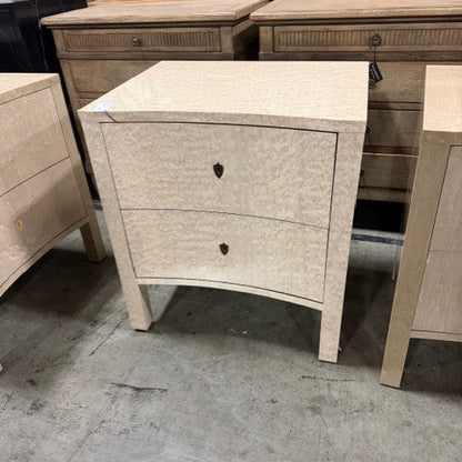 Light wood nightstand with two drawers featuring curved front design and tapered legs. Natural wood grain visible with keyhole-style drawer pulls. Part of matching bedroom furniture set.