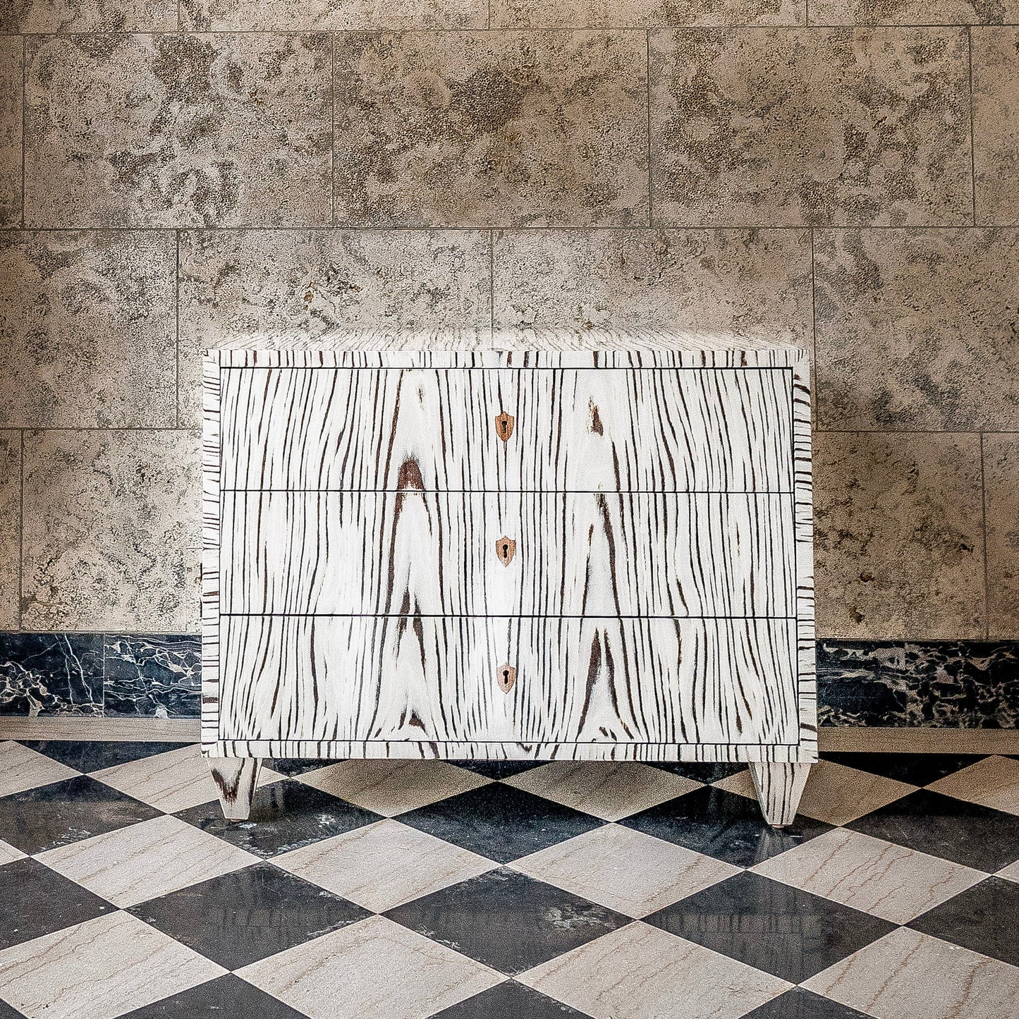 White wood grain chest of drawers with three drawers and brass hardware, featuring distinctive black wood grain pattern and fringe detailing on marble checkered floor