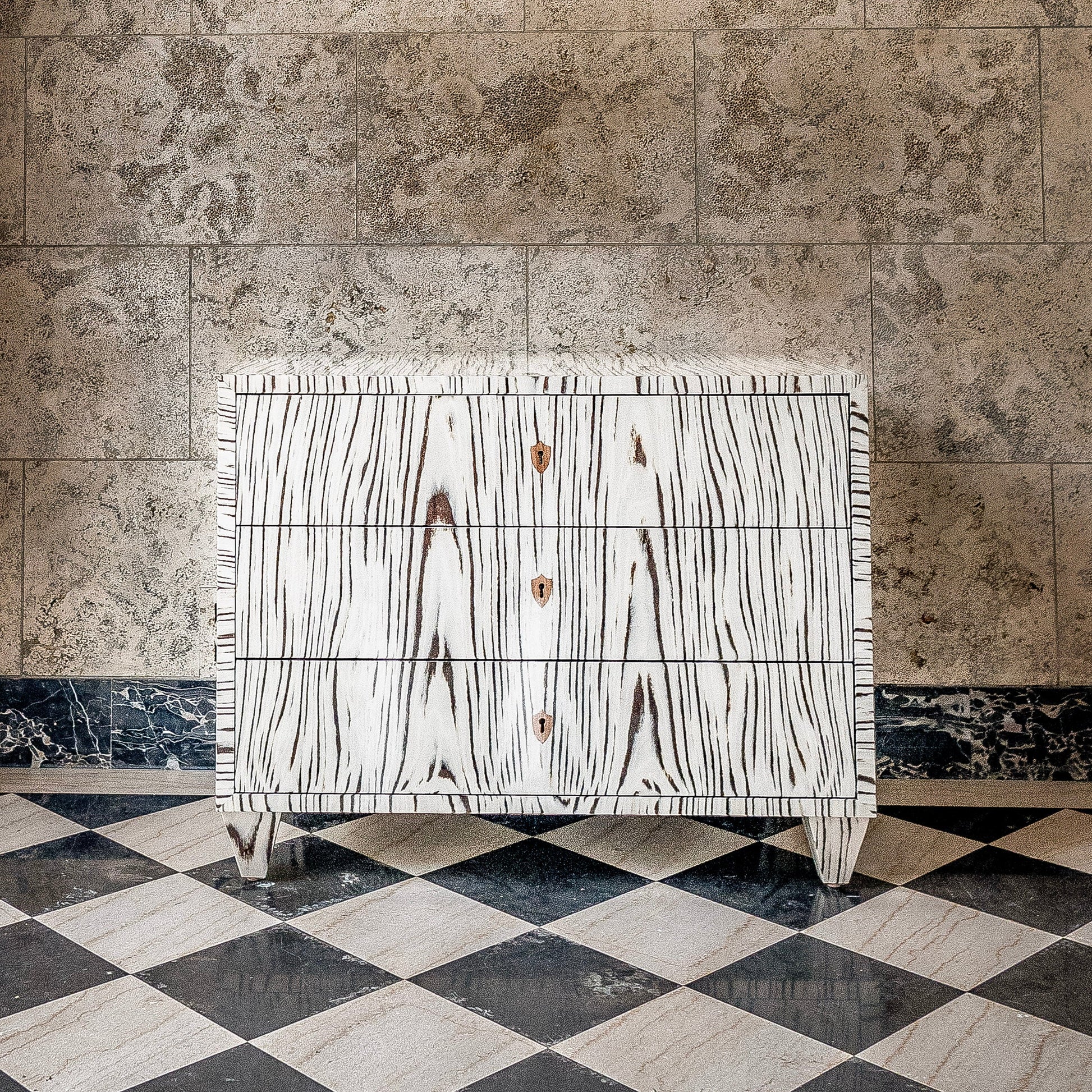 White wood grain chest of drawers with three drawers and brass hardware, featuring distinctive black wood grain pattern and fringe detailing on marble checkered floor