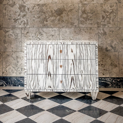 White wood grain chest of drawers with three drawers and brass hardware, featuring distinctive black wood grain pattern and fringe detailing on marble checkered floor