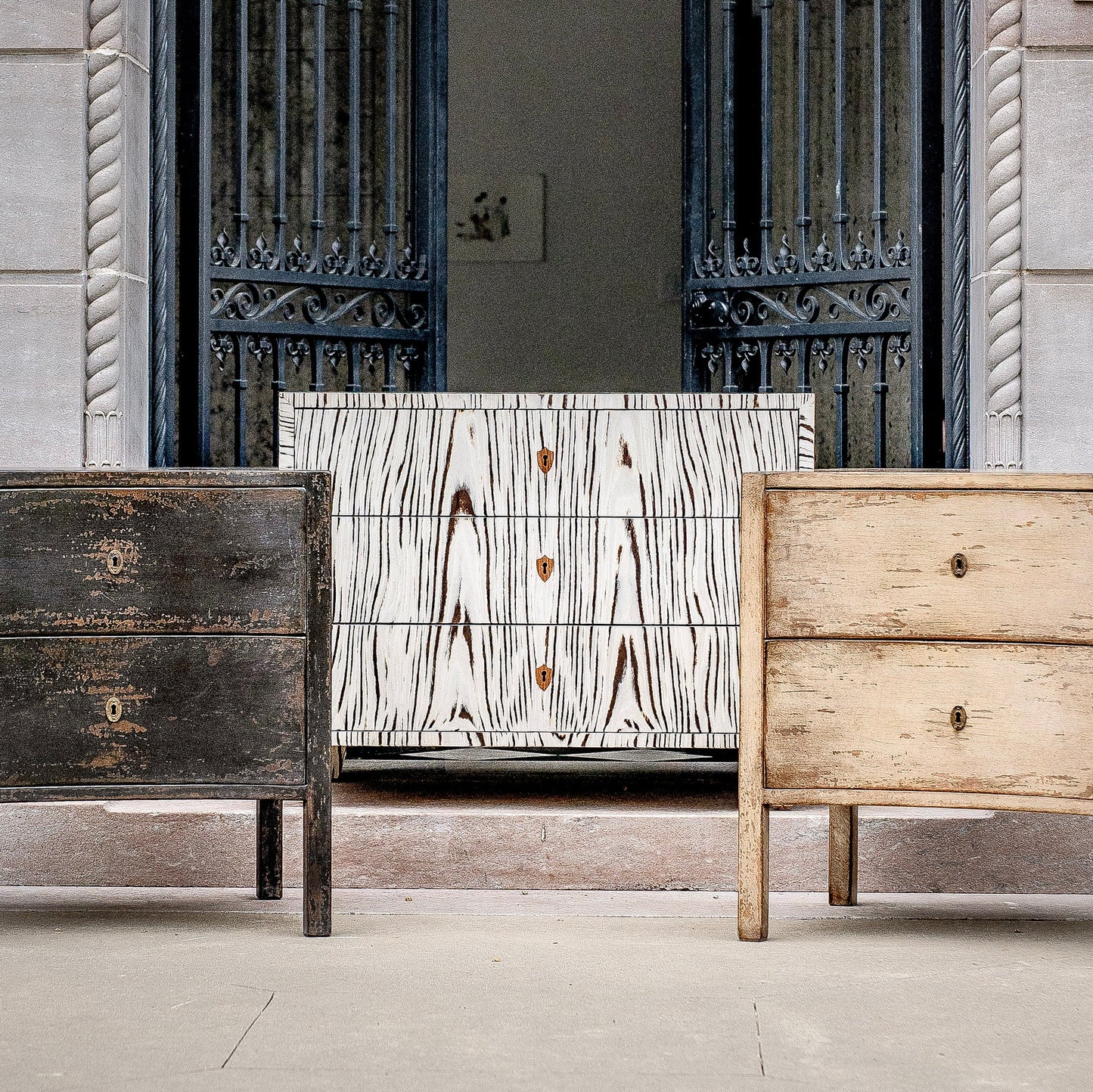 Three chest of drawers displayed together showing different finishes - dark distressed wood on left, white with black wood grain pattern in center, and natural light wood on right