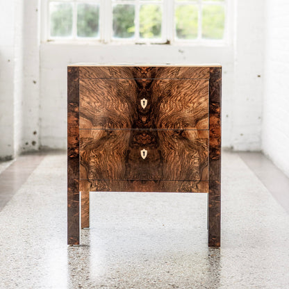 Elegant walnut burl wood chest with two drawers featuring dramatic grain patterns and brass keyhole escutcheons, supported by four slender legs in a contemporary design
