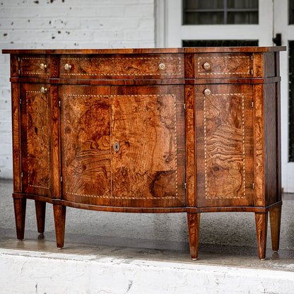 Traditional sideboard buffet in rich burled walnut wood with distinctive swirled grain patterns. Features four cabinet doors, three drawers with brass knobs, and tapered legs.