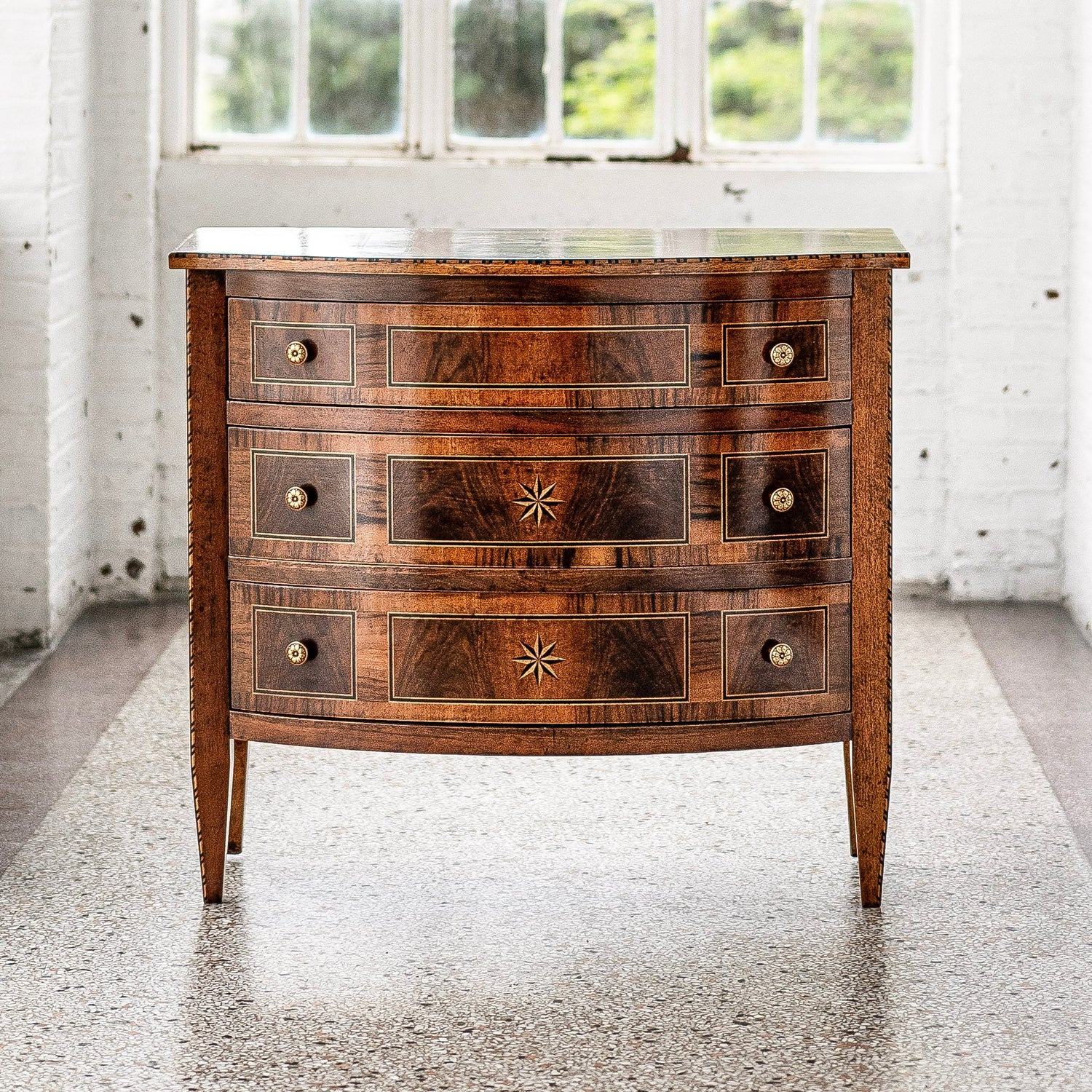Antique-style walnut chest of drawers with three curved front drawers, decorative star inlays, brass hardware, and light wood string inlay trim on tapered legs