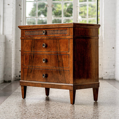 Traditional wooden chest with rich brown finish featuring four drawers including decorative fluted top drawer, brass hardware, and tapered legs on polished concrete floor