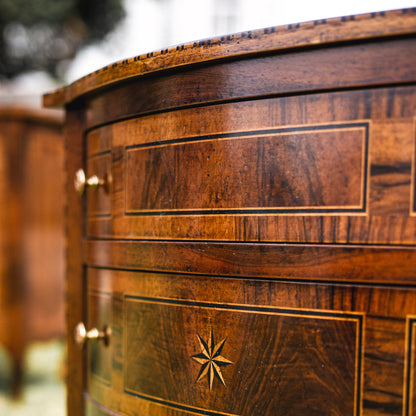 Curved wooden chest with rich brown mahogany finish featuring decorative inlay work, geometric star motif, brass hardware, and elegant banding details on drawer fronts