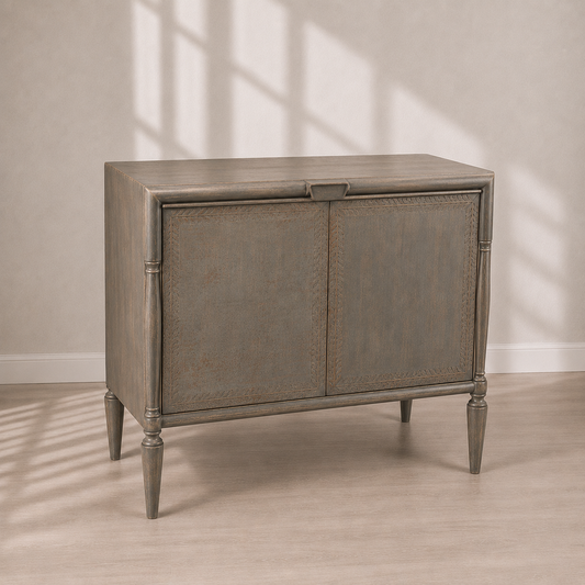 Distressed gray-brown wood accent cabinet with carved leaf border door panels, turned spindle corner posts, tapered legs, and center pull hardware