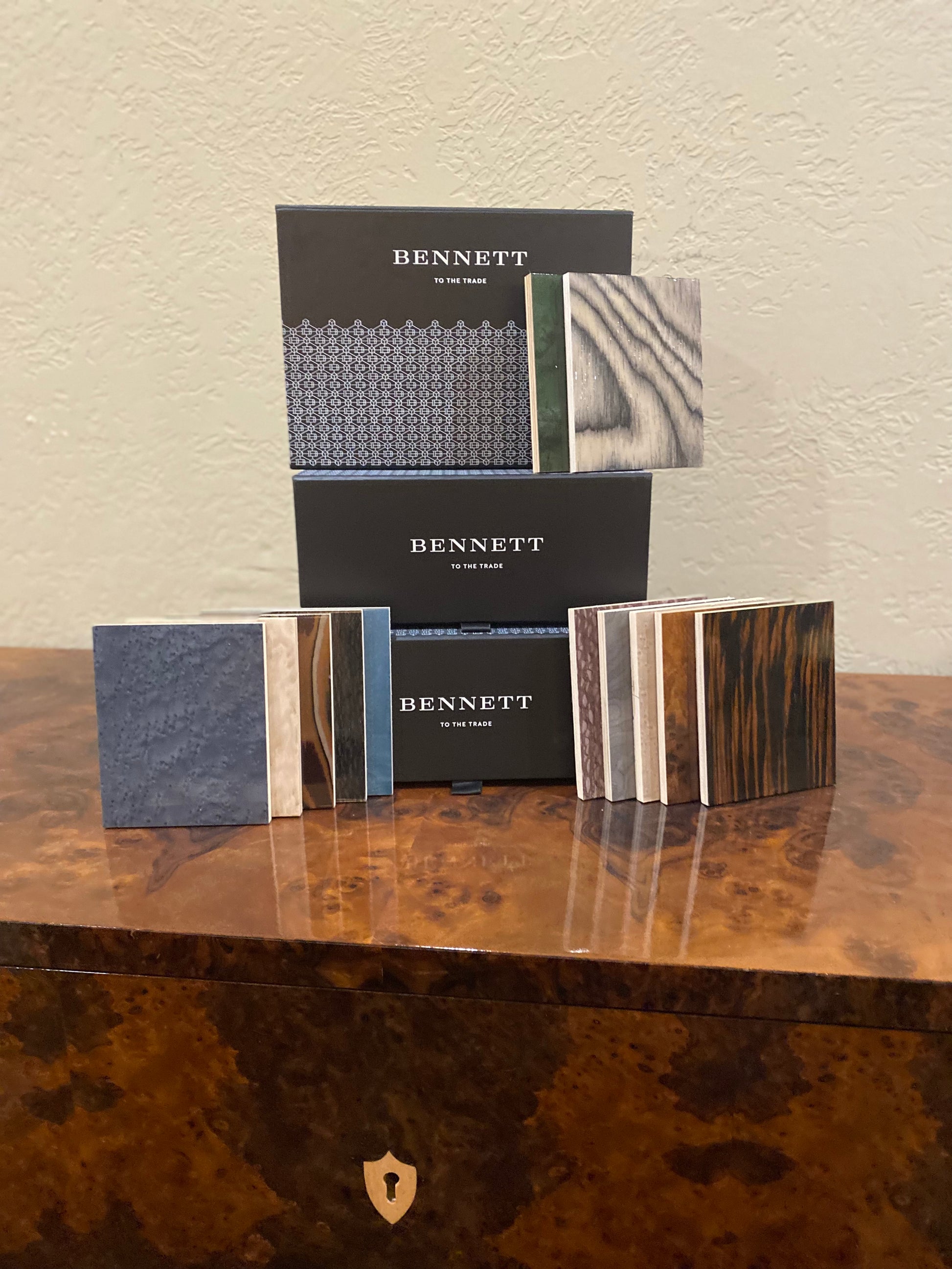 Bennett veneer finish samples displayed on polished burl wood table, showing various wood grain patterns including dark slate, natural maple, and rich walnut finishes in sample squares