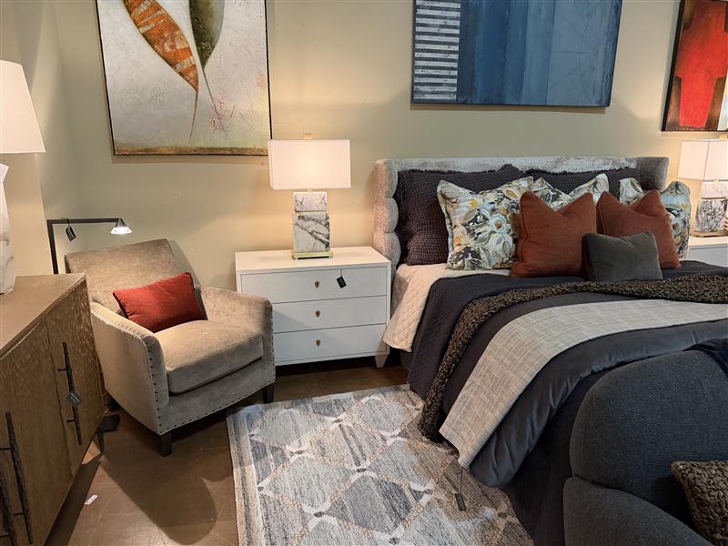 White modern chest of drawers with three drawers and sleek handles, positioned as bedside table in contemporary bedroom setting with gray upholstered headboard and neutral decor