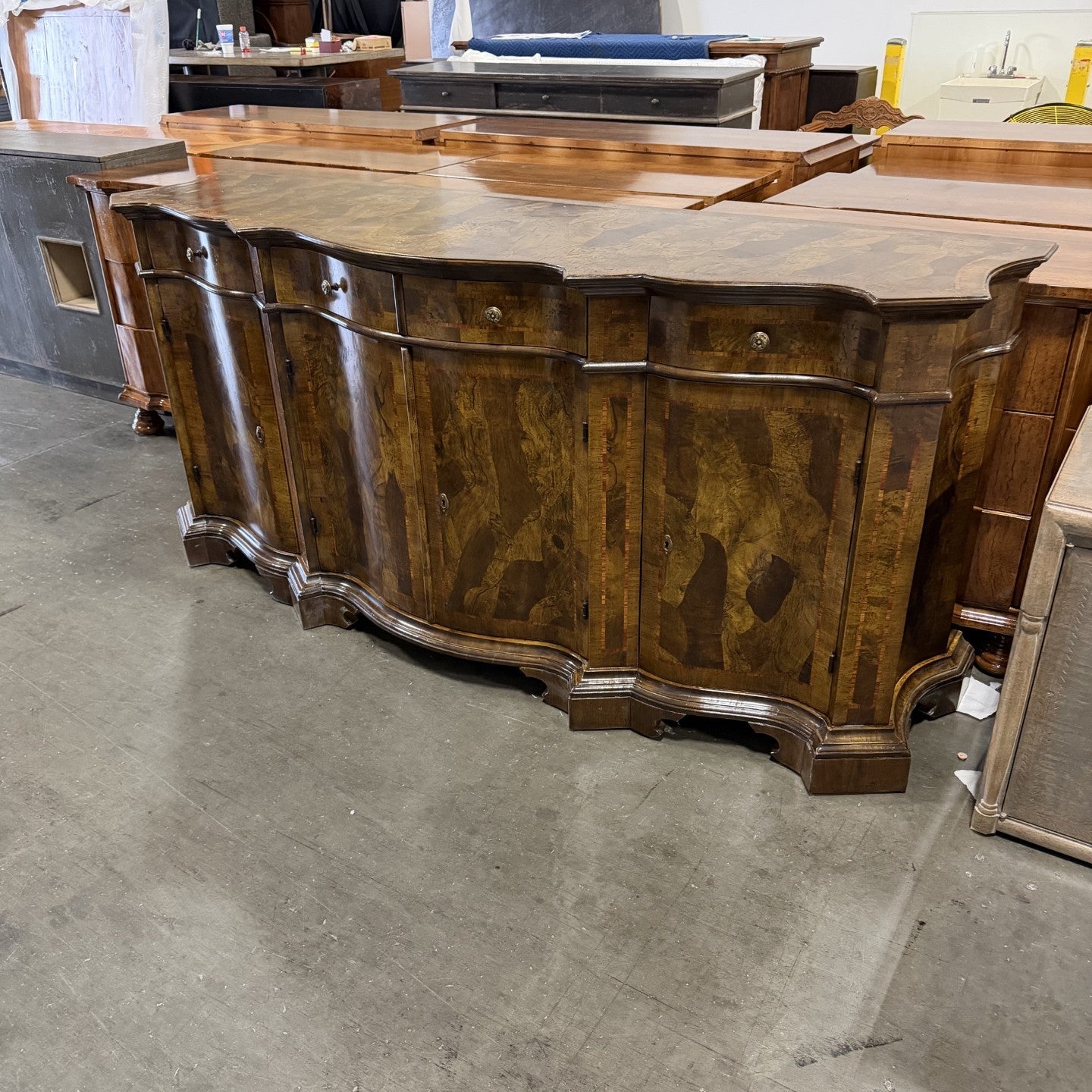Traditional curved sideboard buffet in rich walnut wood with ornate burl wood veneer panels, featuring multiple cabinet doors, decorative carved legs, and scalloped edges