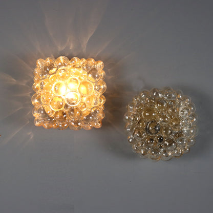Pair of vintage bubble glass wall sconces, one illuminated casting warm amber glow with starburst shadow pattern, one unlit, featuring textured spherical glass shade