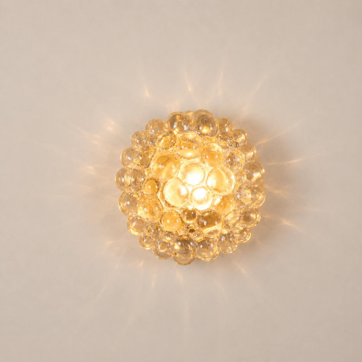 Globe-shaped wall sconce with clustered clear glass bubbles casting starburst light patterns on a neutral wall, warm amber glow from central bulb