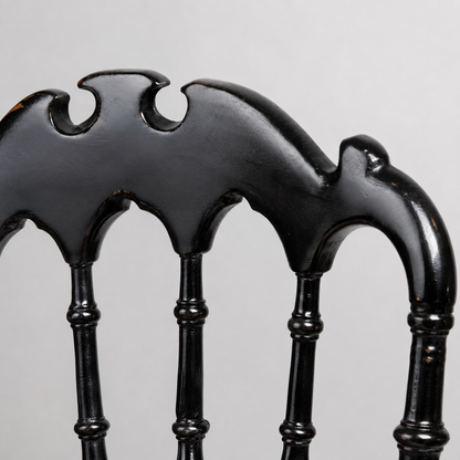 Black ebonized wood chair back detail featuring Gothic arch spindles and decorative carved crest rail with bat-wing silhouette cutouts, distressed finish