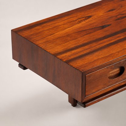 Mid-Century modern low-profile coffee table in rich warm walnut wood with carved pull drawer, small cylindrical legs, and smooth satin finish showcasing natural grain
