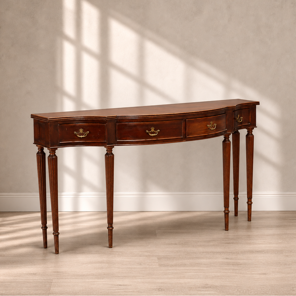 Traditional mahogany console table with curved serpentine front, four drawers with ornate brass drop pulls, and six reeded tapered legs in rich warm brown finish.