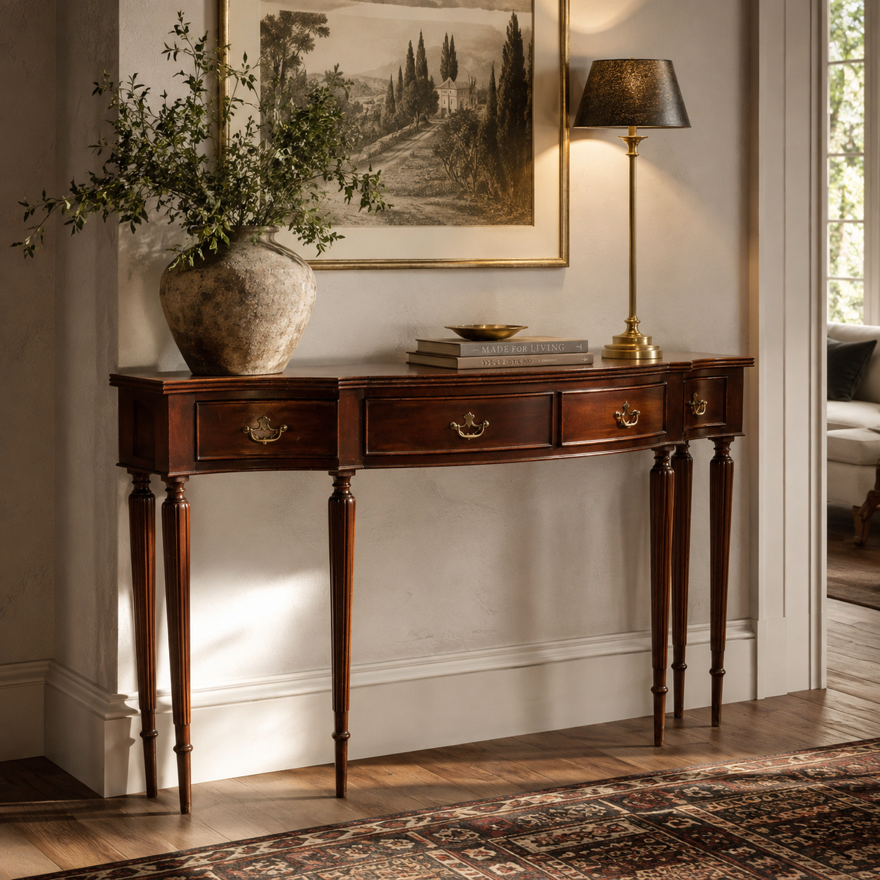 Traditional mahogany console table with serpentine front, three brass bail-pull drawers, and slender reeded tapered legs, styled with ceramic vase and brass lamp.