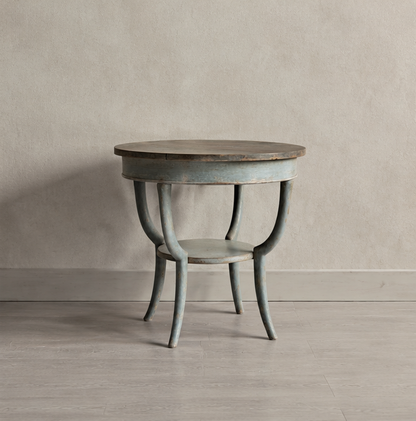 Round occasional table with weathered gray painted finish and curved legs. Features a darker wood top contrasting with the painted base in a vintage-inspired design.